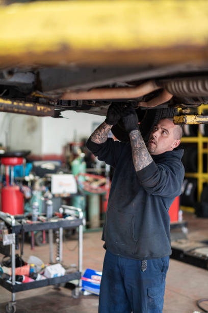 reparaturmeister - automechaniker, kaukasischer weißer mann mit tätowierungen an den händen, arbeiten in einer autowerkstatt - befestigung aufhängung des autos auf dem aufzug erhöht. - vertical lift bridge stock-fotos und bilder