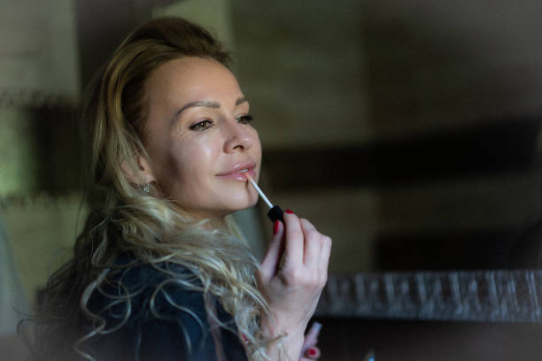 Beautiful adult woman is puts lip gloss in bathroom