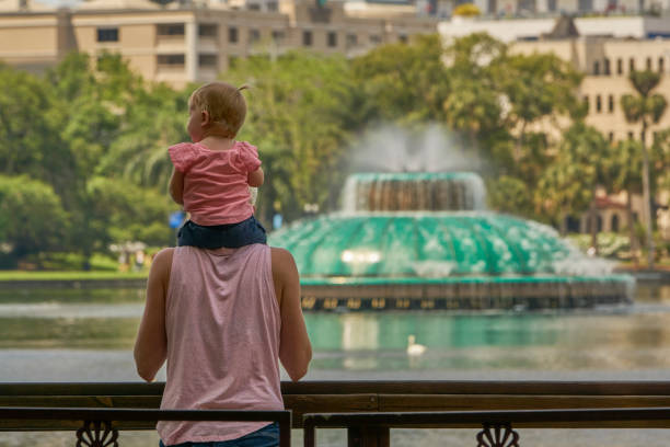 Mother and Baby Daughter at Lake Eola Park and the Orlando Skyline in Downtown Orlando Florida USA Mother and baby daughter at Lake Eola Park in downtown Orlando Florida. lake eola stock pictures, royalty-free photos & images