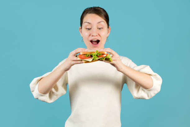 a young woman sends a sandwich to her mouth - eating sandwich emotional stress food imagens e fotografias de stock