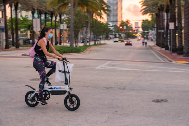 Woman Wearing Face Masks Bike Riding on Ocean Drive in South Beach Miami During Coronavirus Pandemic In Miami Beach, United States a woman wearing a protective face mask rides along Ocean Drive in South Beach as the sunsets during the Coronavirus pandemic. 1 hotel south beach stock pictures, royalty-free photos & images