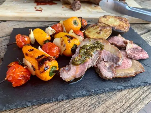 Picanha (top sirloin) steak sliced on slate plate with vegetable skewers, roasted potatoes and Chimichurri