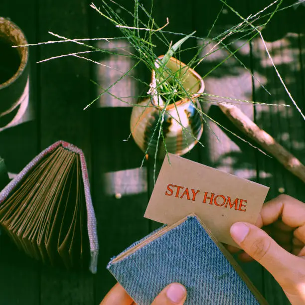 Top view outdoor table at morning with woman hand hold a piece of paper with STAY HOME message in epidemic season by corona virus, notebook, pencil ready for work at home in social quarantine period