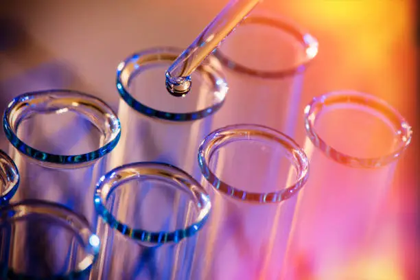 Test tube row. Concept of medical or science laboratory, liquid drop droplet with dropper in blue red tone background, close up, macro photography picture.