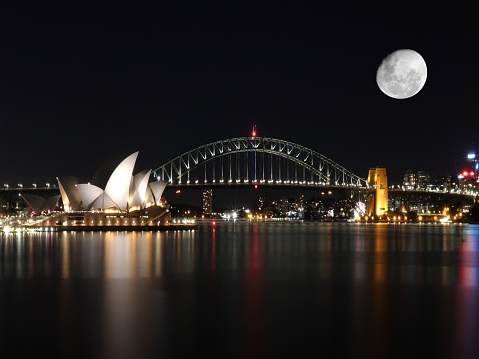 Sydney harbour bridge illuminated by the moon and circular quay with vibrant colourful of the moon and lights at midnight in NSW Australia