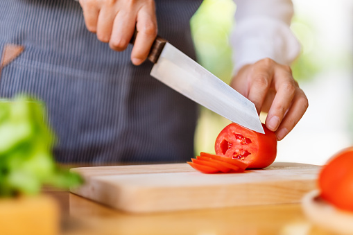 Closeup image of a woman chef cutting and chopping tomato by knife on wooden board