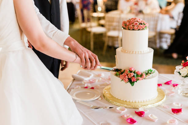 istock Bride and Groom Cutting a Wedding Cake Adorned with Pink Flowers Icing 1220482575