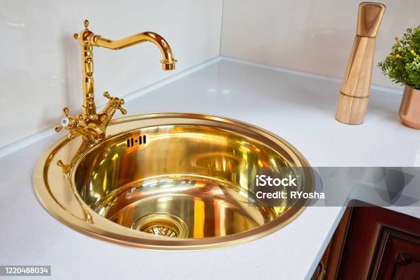 Kitchen Luxurious Interior With Golden Brass Sink And Faucet Double Tap Mixer In Modern Contemporary Design With Stone Marble Countertop Cherry Hardwood Panels Pepper Mill And Flower Pot Stock Photo - Download Image Now