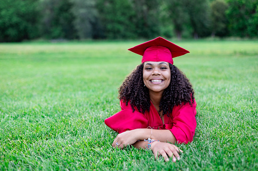 Portrait of a beautiful multiethnic woman in her graduation cap and gown. Smiling and cheerful as she poses lying in the grass