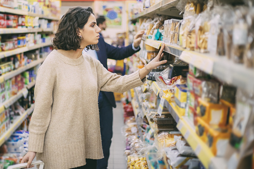 Serious woman looking at cookies in grocery store. Side view of people choosing baked goods in supermarket, selective focus. Shopping concept