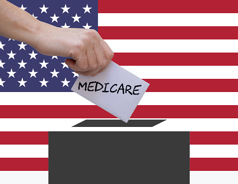 Female hand voting against american flag background. Medicare is written on the ballot paper