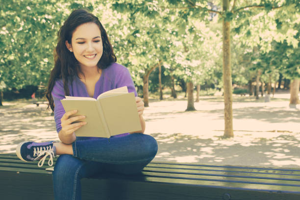 istock Beautiful smiling student reading book in park 1220495516