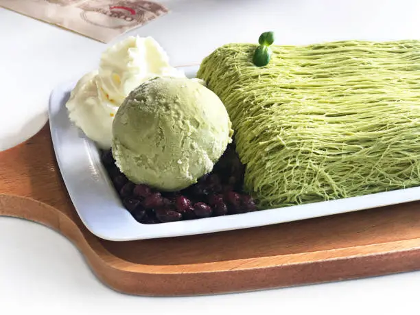 Photo of Close up Shiltarae Bingsu matcha green tea with green tea ice cream whipped topping and red bean caramel, put on white plate and wooden tray, THAI sweet dessert style, good and healthy for freshness.