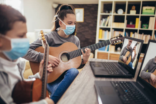 Boy and girl playing acoustic guitar Boy and girl, wear protective masks, playing acoustic guitar and watching online course on laptop while practicing at home. Online training, online classes. string instrument photos stock pictures, royalty-free photos & images
