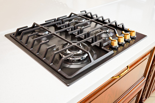 Modern hob gas stove made of steel and cast iron, with golden controls using natural gas or propane for cooking products on light countertop in kitchen interior
