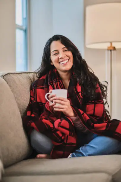 Young latin woman cozy at sofa at home holding a coffee mug