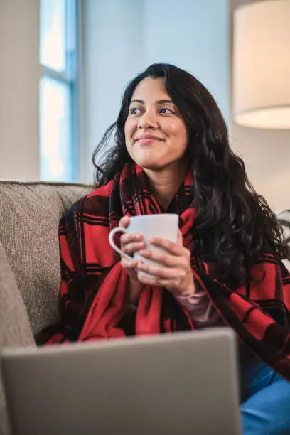 Young latin woman cozy at sofa at home holding a coffee mug