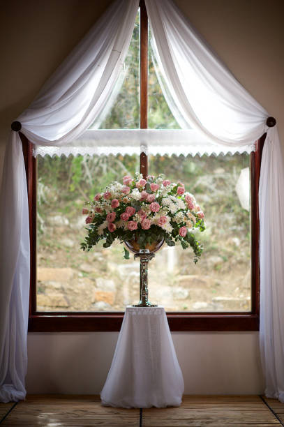 istock Rose Wedding Flower arrangement in front of Window with white draping 1220504045