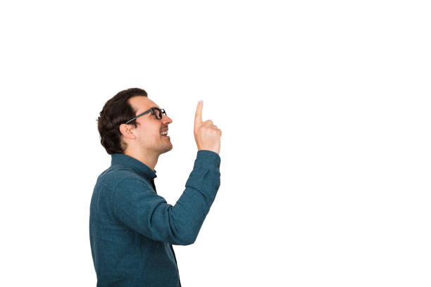 Side view of young businessman keeps index finger up, eureka gesture, isolated over white background with copy space. Business worker wears glasses looking up cheerful, thinking of new ideas.