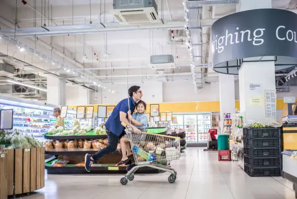 An Asia Chinese girl sitting in a shopping cart being pushed by her father. They having fun in supermarket.