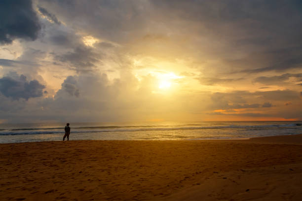istock Man silhouette stand alone on stony beach and watching romantic colorful sunrise. 1220505336
