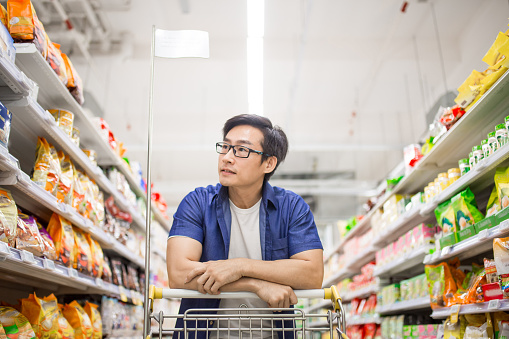 An Asia mature man pushes shopping cart and browses for products in groceries shop.