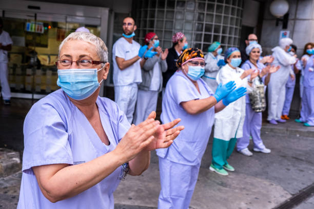 Health workers applauding. Coronavirus reaction in Valencia, Spain Valencia, Spain; 20th apr 2020: Some workers of the 'Hospital Clínico Universitario' meet at the door of the hospital to applaud together with the neighbours as every day at 8 pm since the beginning of the lockdown due to the Covid 19 pandemic editorial stock pictures, royalty-free photos & images
