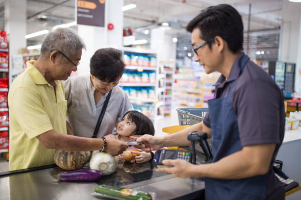 starszy mężczyzna płaci przy kasie w supermarkecie. towarzyszy mu żona i wnuk. - cash register paying checkout counter cashier zdjęcia i obrazy z banku zdjęć