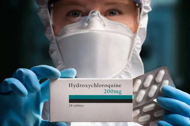 Photo of Doctor in protective equipment holding hydroxychloroquine pills