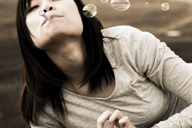 istock Young woman lying outdoors and facing upwards and blowing soap bubbles. 1220513583