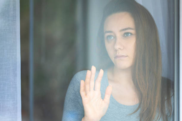 istock Thoughtful young woman looking through window 1220515149