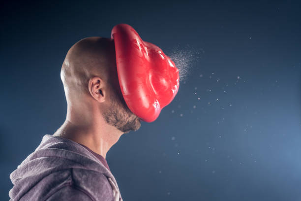Water balloon exploding on man's face Red water filled balloon exploding on man's face against grey background. water balloon stock pictures, royalty-free photos & images