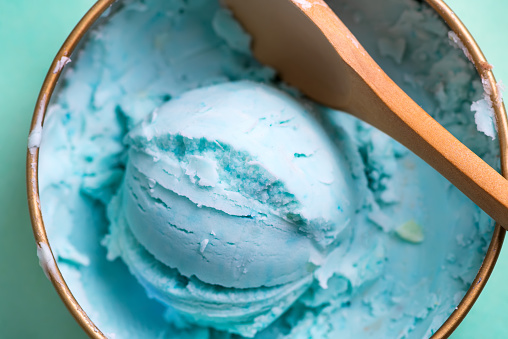 Close-up bowl with freshly cooked homemade cold natural ice cream or gelato blue color with spoon on a light blue background, copy space. Top view.