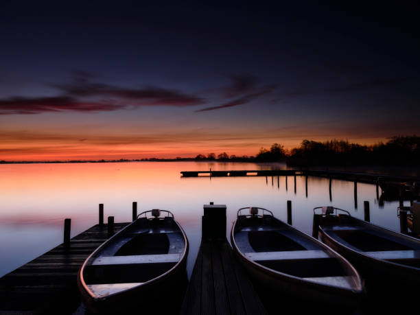 Small motorboats lying still at a platform under colourful dawn in a calm lake Leekstermeer, the Netherlands .