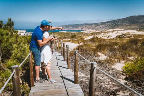 Photo of Adult female tourist enjoying costal view of Praia do Guincho Beach. Cascais, Portugal. This is popular blue flag Atlantic beach for surfing, windsurfing, and kitesurfing