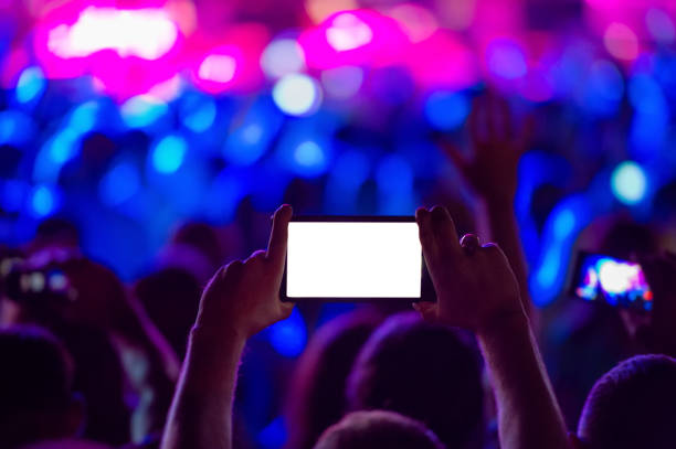 ムイクロックコンサート中に写真を撮っている間、携帯電話を持つ音楽ファンの手がオンになっています。 - popular music concert mobile phone smart phone telephone ストックフォトと画像