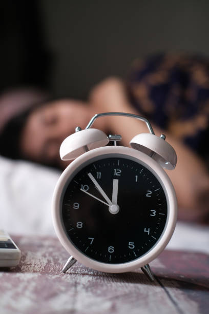 Alarm clock on table with woman sleeping on background