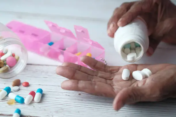 Photo of Elderly woman pouring pills from bottle on hand, top view