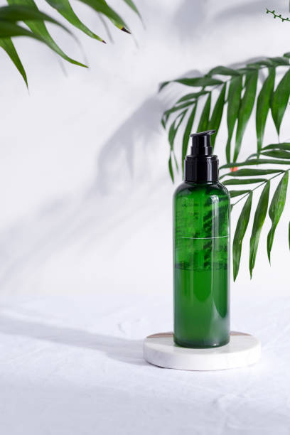istock Plastic green bottle with natural lotion for clean skin on a white textile background wit green tropical leaves. 1220523172