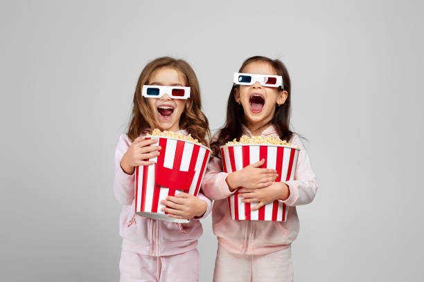 two little girls in red-blue 3d glasses holding popcorn buckets - surprise child little girls shock imagens e fotografias de stock