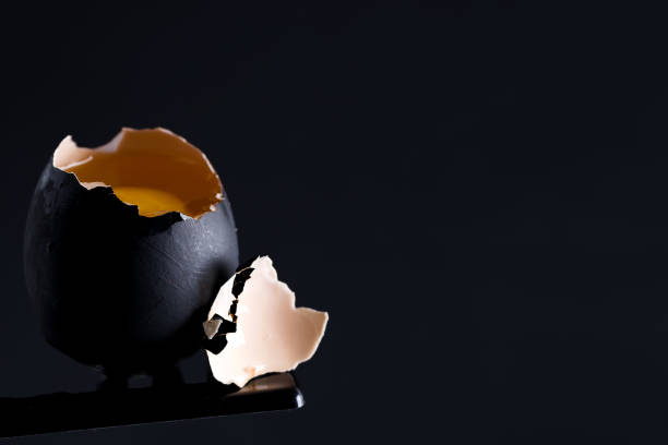 istock Black painted broken raw egg with fresh yellow yolk on the same color background. 1220524664