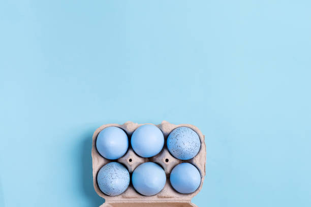 istock Papercraft container with handmade painted pastel blue Easter eggs on a same color background. Flat lay. 1220527452