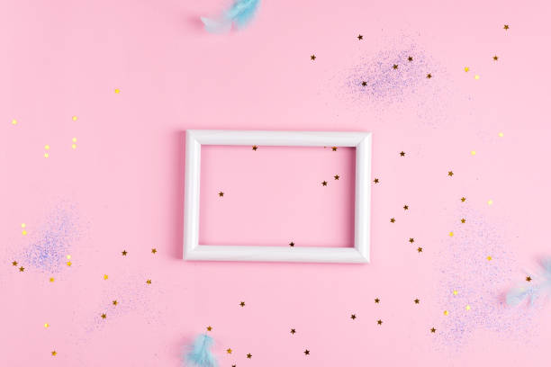 istock Festive frame with light colored bird's feathers and confetti decoration on a light pink background. 1220527707