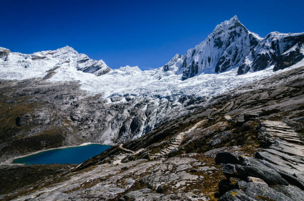 estrada rochosa ao lado de altas montanhas nevadas de taulliraju e lagoa taullicocha, no trekking da quebrada santa cruz no peru - mountain peru cordillera blanca mountain range - fotografias e filmes do acervo