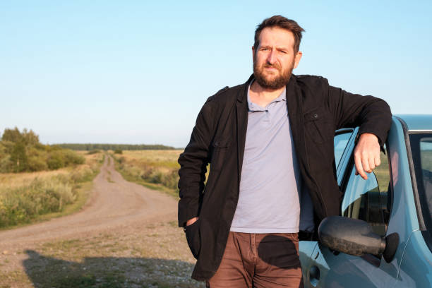 istock a white man with a beard stands by the car with his elbows on the roof 1220531339