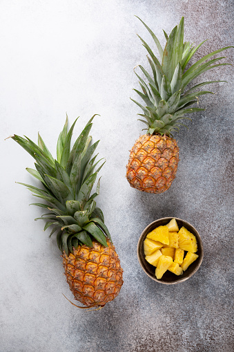 Two whole fresh ripe pineapples and bowl with chopped pineapple  on concrete background. Food background. Top view, copy space.