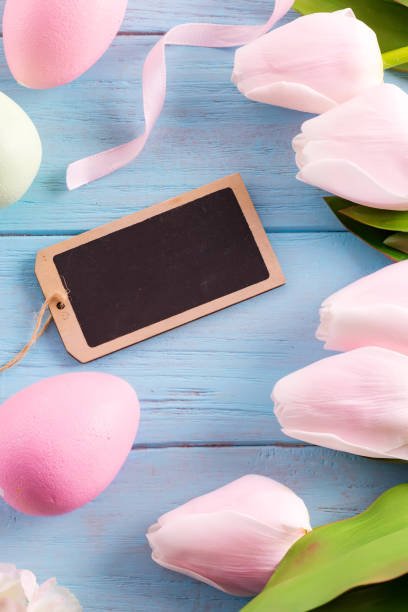 istock Holiday card with fresh tender tulips frame and chalkboard for message on a pastel blue wooden background. 1220534841