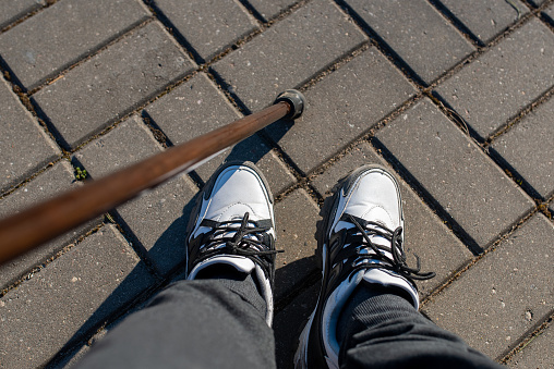 Legs of a young guy in sneakers, with a cane for walking.