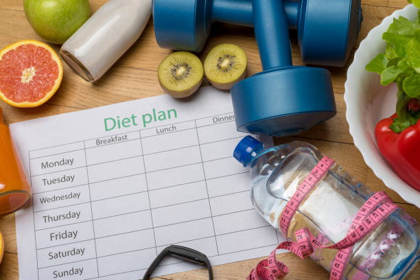istock Diet plan, menu or program, roulette, water, dumbbells and diet food with fresh fruit on wooden floor. 1220540355