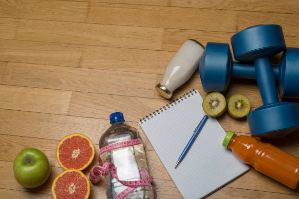 istock Training, exercise, cheerfulness and health - two plastic dumbbells, a notebook, mineral water with juice, fruit and a pen on the wooden floor. 1220540358